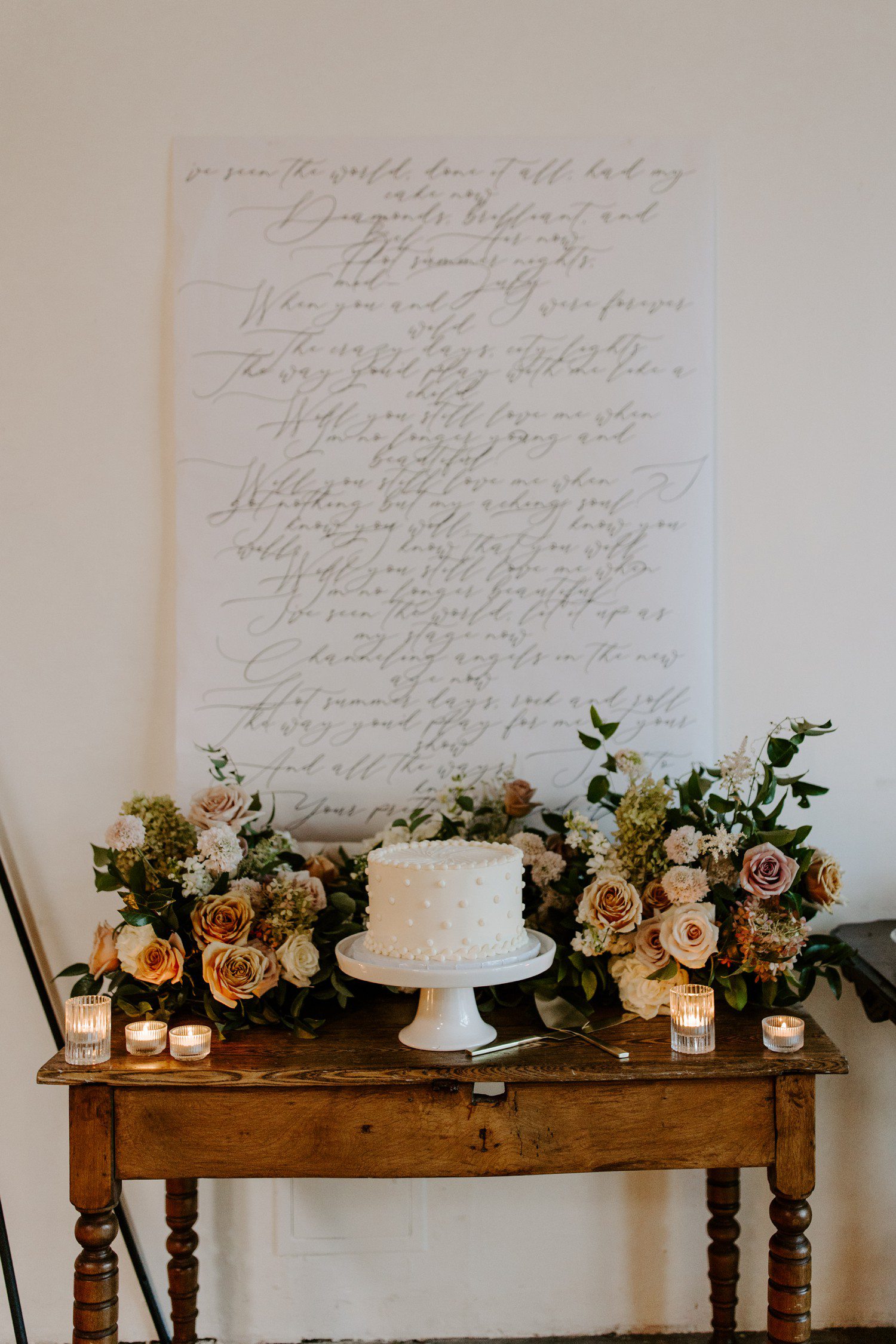 Small wedding cake table with florals and script sign.