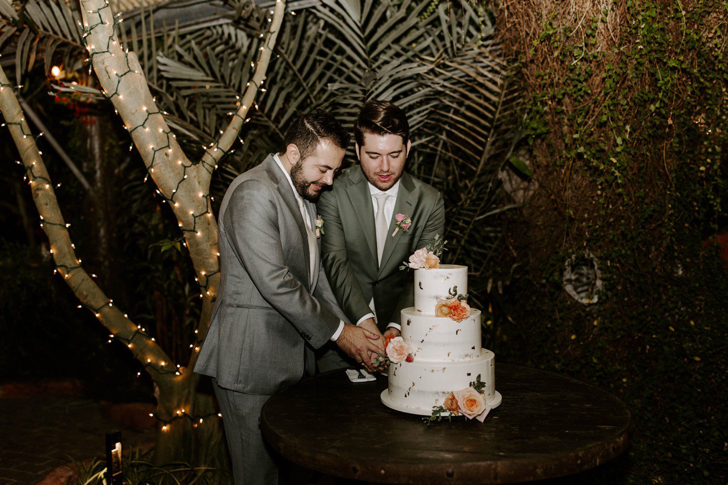 Grooms cutting wedding cake together.