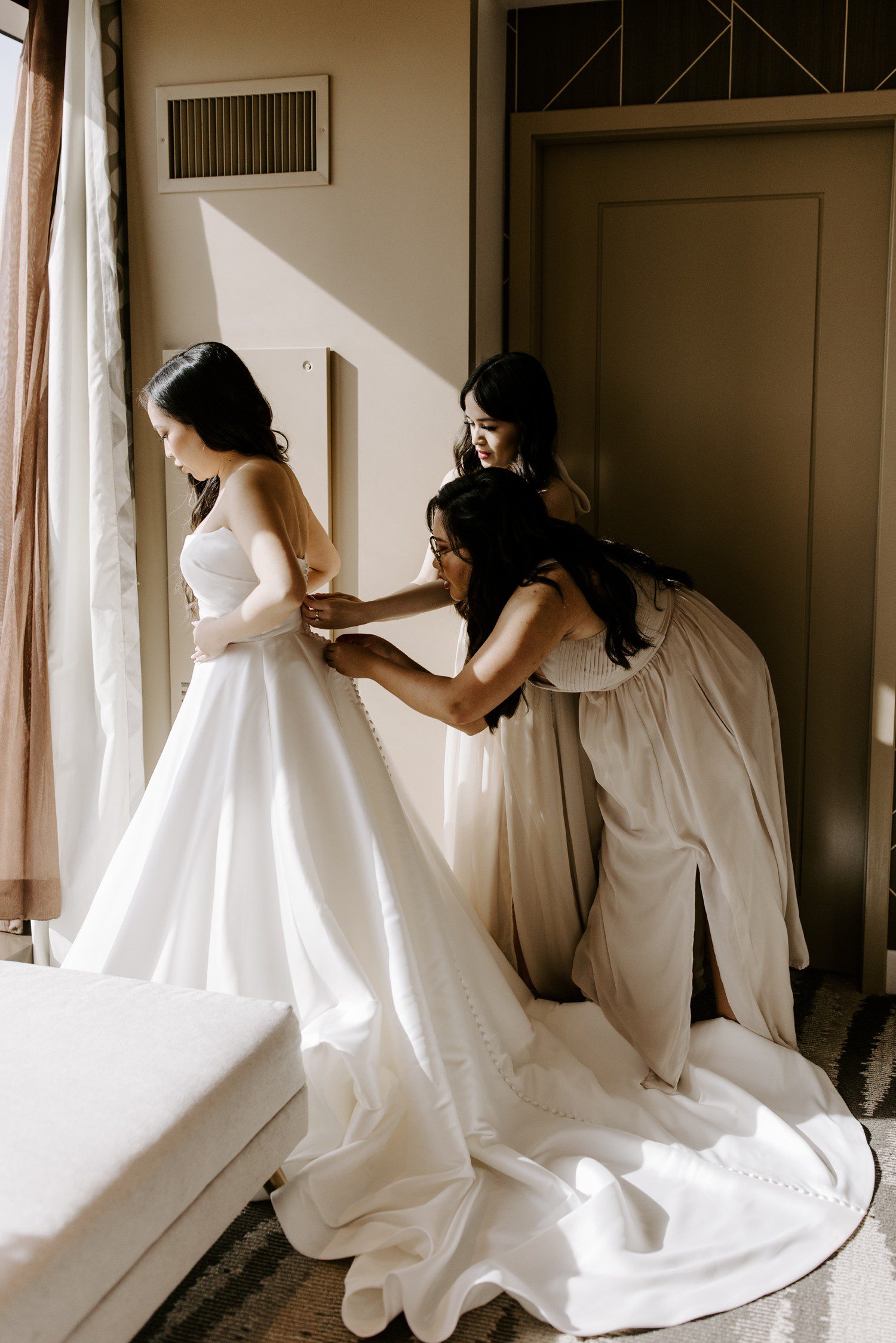 Bridesmaids helping zip bride into dress.