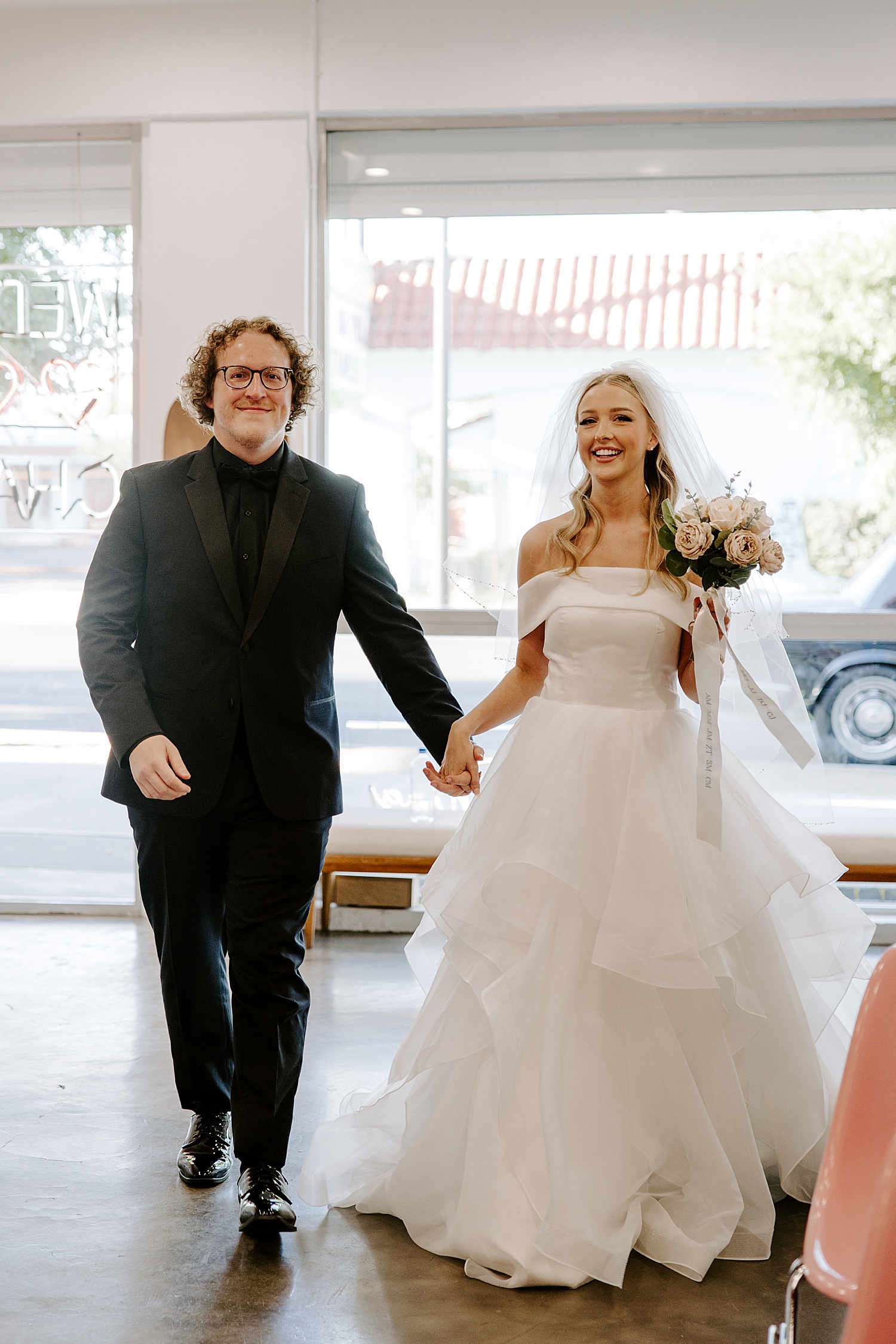 blonde woman in white dress walks with man in black suit by Katelyn Faye Photography