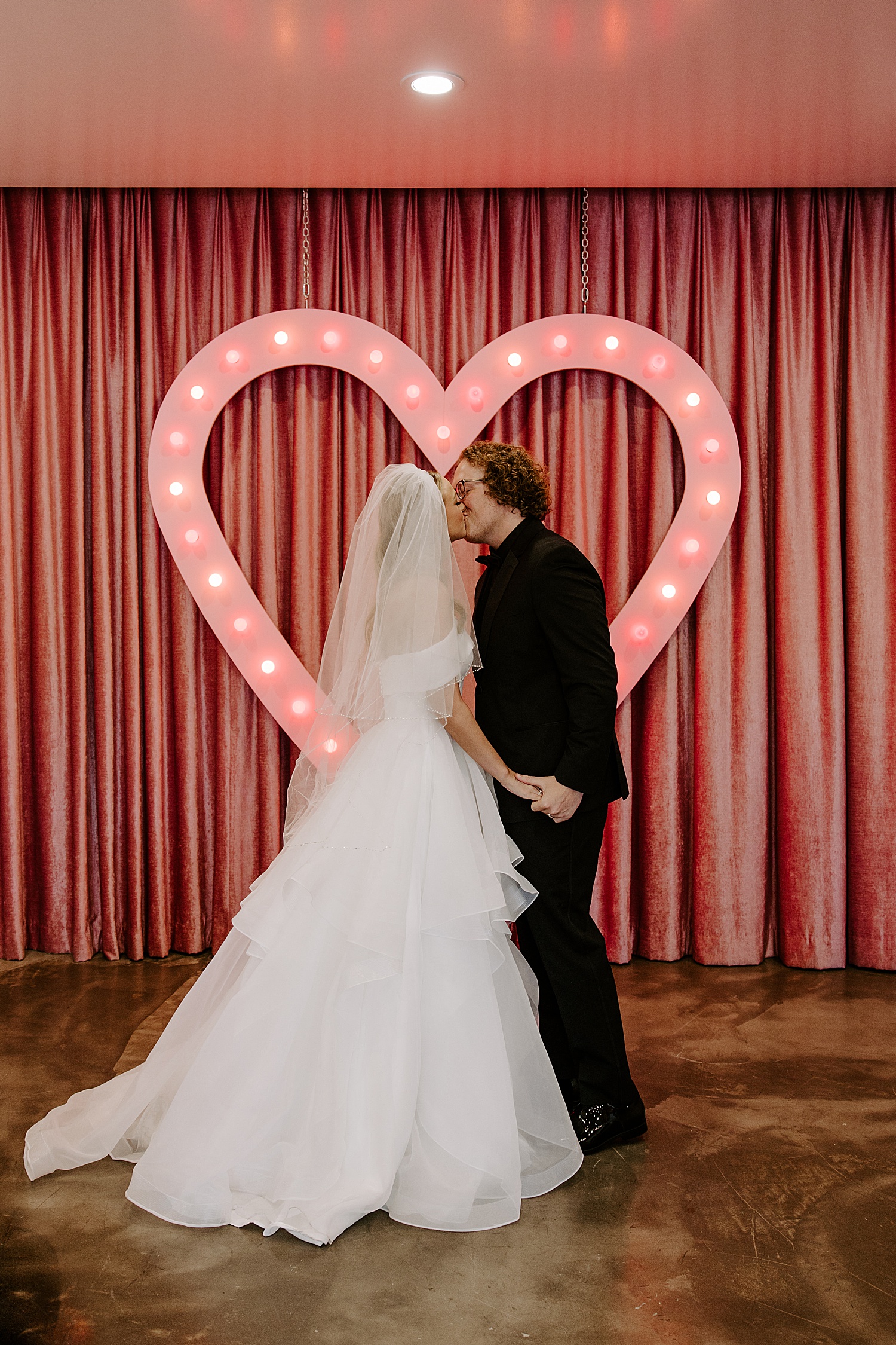 newlyweds kiss under light up heart at Sure Thing Chapel