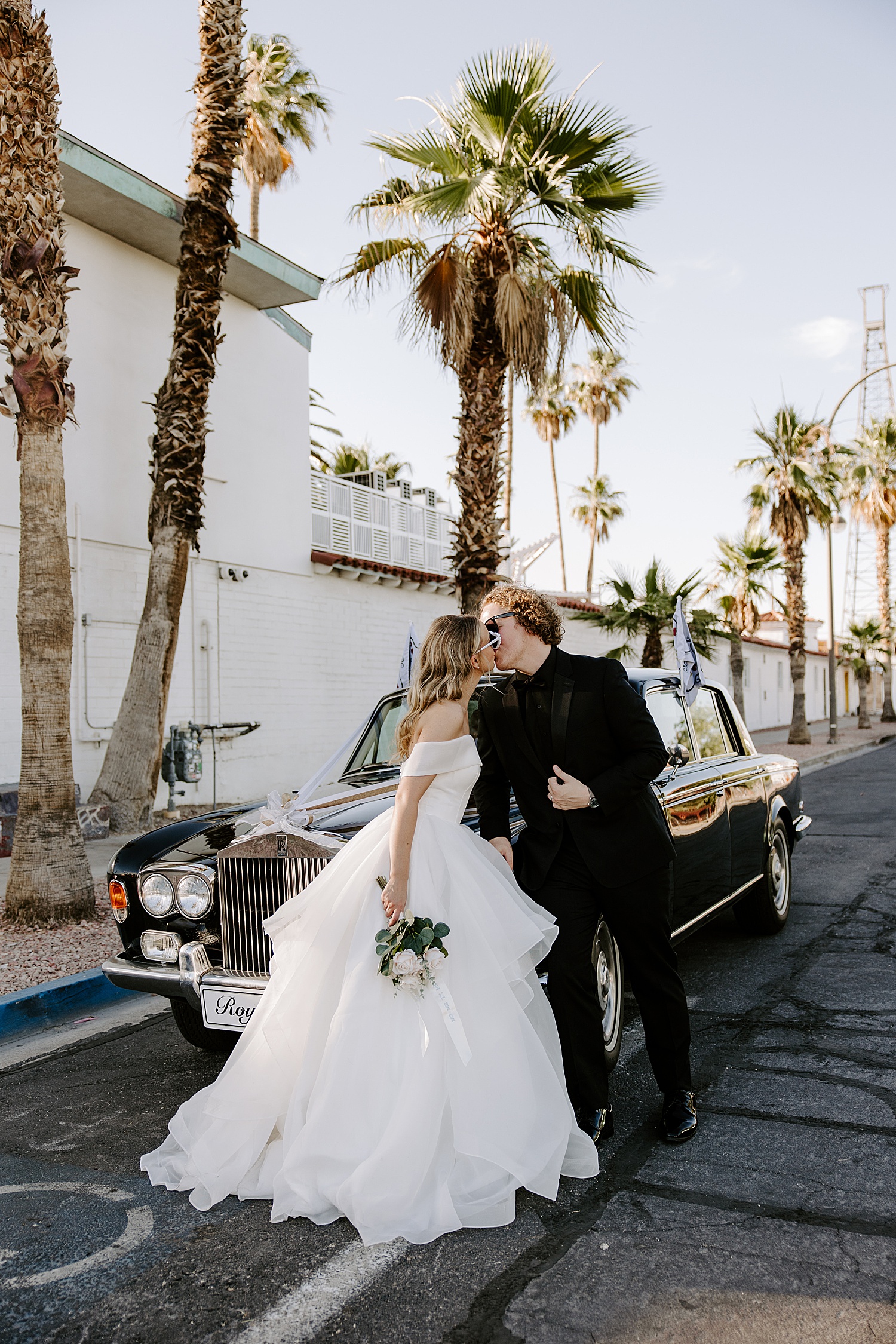 blonde woman in white gown kisses her man over old car by Las Vegas elopement photographer