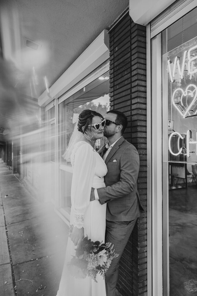 man kisses wife as he leans against Sure Thing Chapel by Katelyn Faye Photography