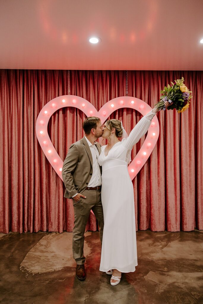 couple kisses in front of light up heart by Las Vegas wedding photographer