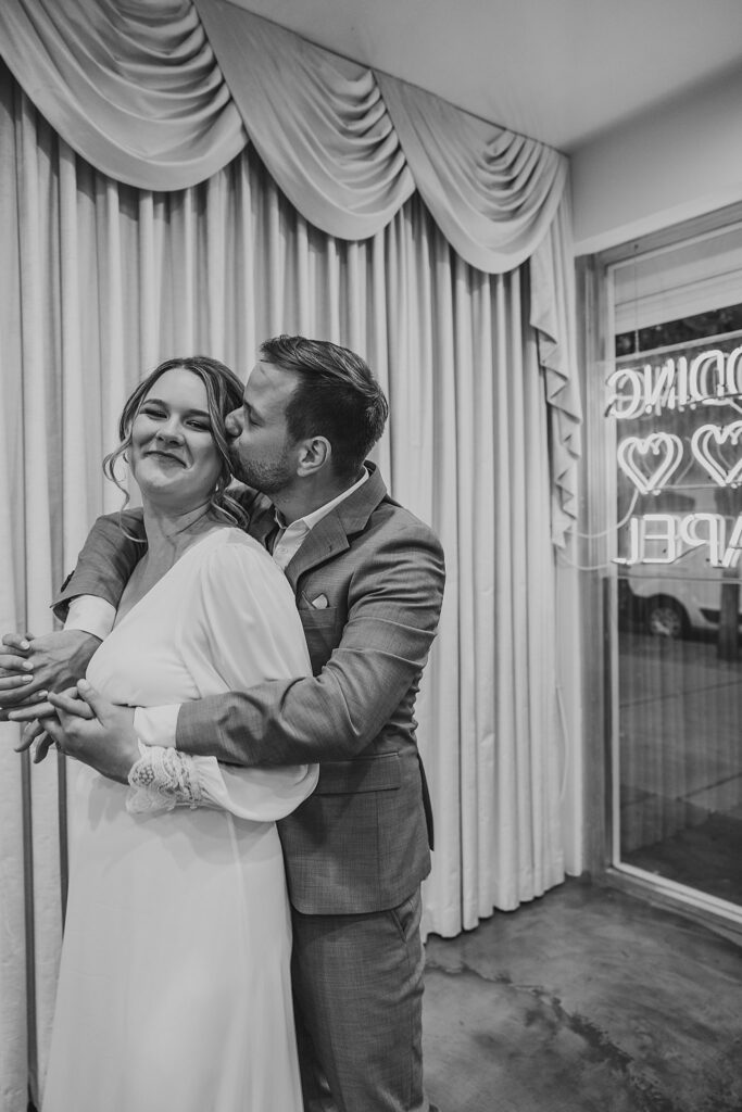 man wraps arms around woman from behind and kisses her cheek by Las Vegas wedding photographer