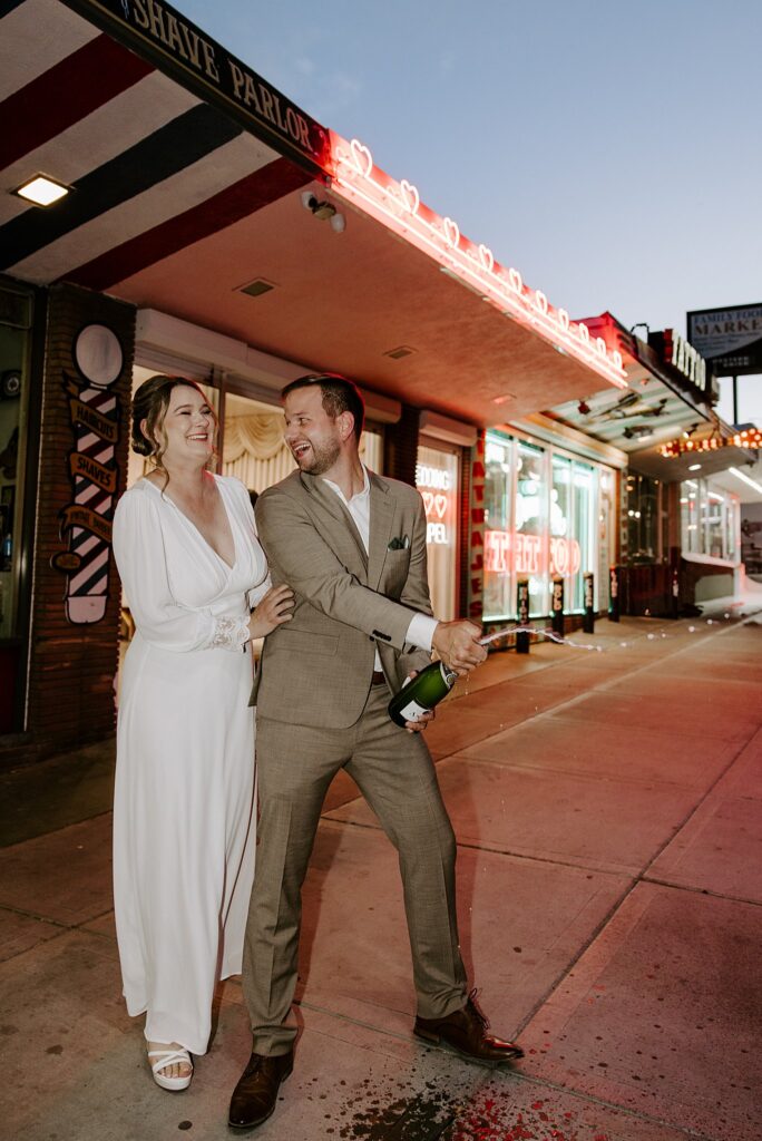 newlyweds pop champagne on sidewalk outside Sure Thing Chapel by Katelyn Faye Photography