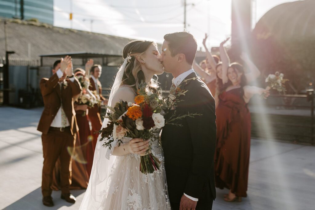 second shooter captures bride and groom kissing in front of wedding party