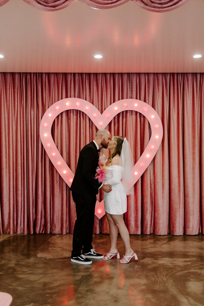 couple kisses in front of pink heart by Las Vegas elopement photographer