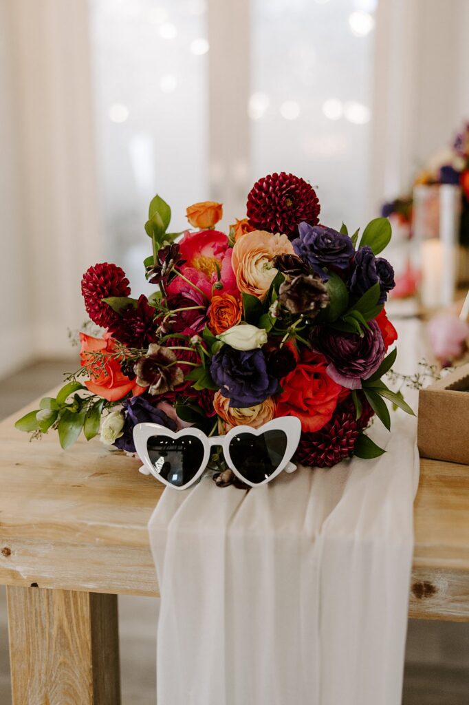 heart shaped sunglasses sit by bright florals at colorful ceremony at Adorn