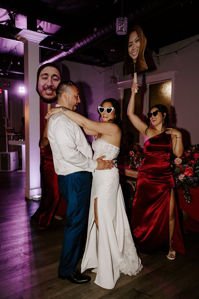 bride and groom dance as bridesmaids hold up face cutouts by Las Vegas wedding photographer