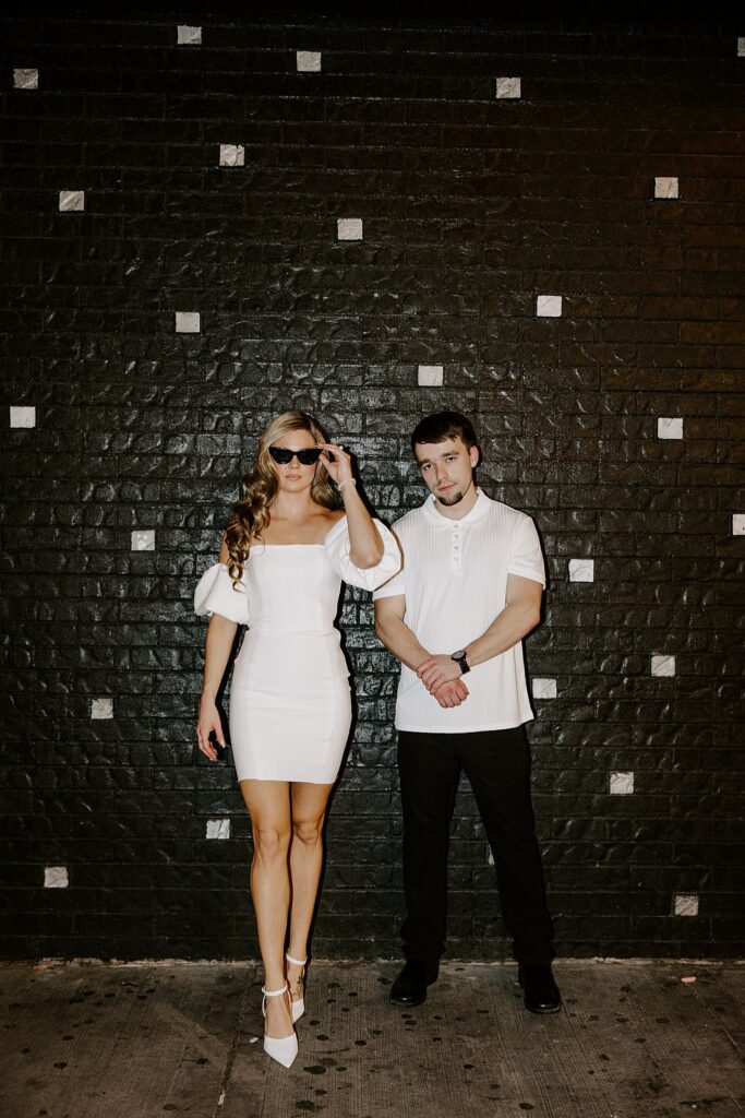 woman in white dress holds sunglasses while man looks straight by Las Vegas wedding photographer