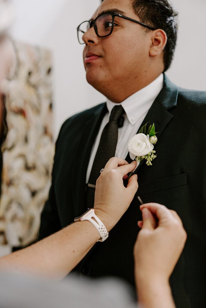 woman pins boutonniere onto groom by Katelyn Faye Photography