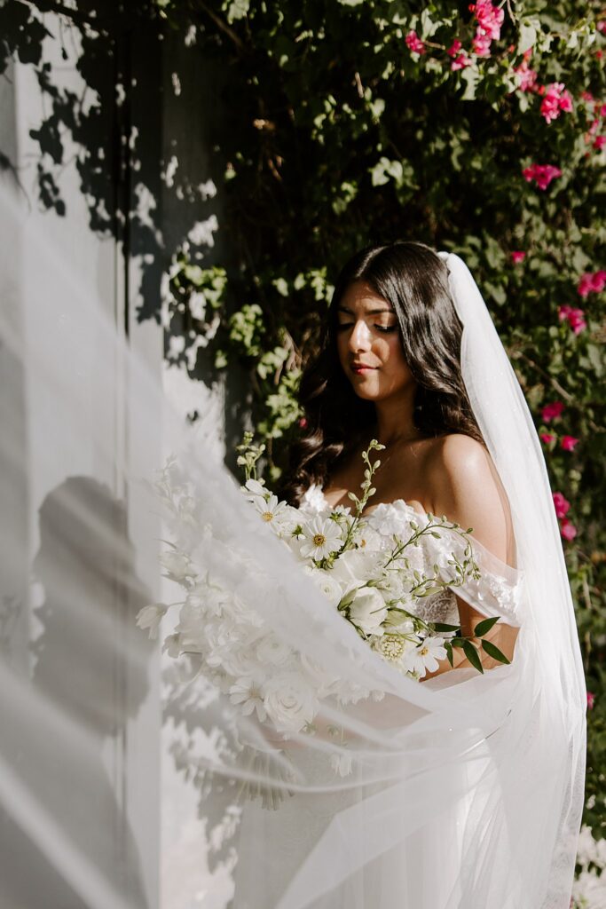 bride holds her florals as veil blows up in wind by Katelyn Faye Photography