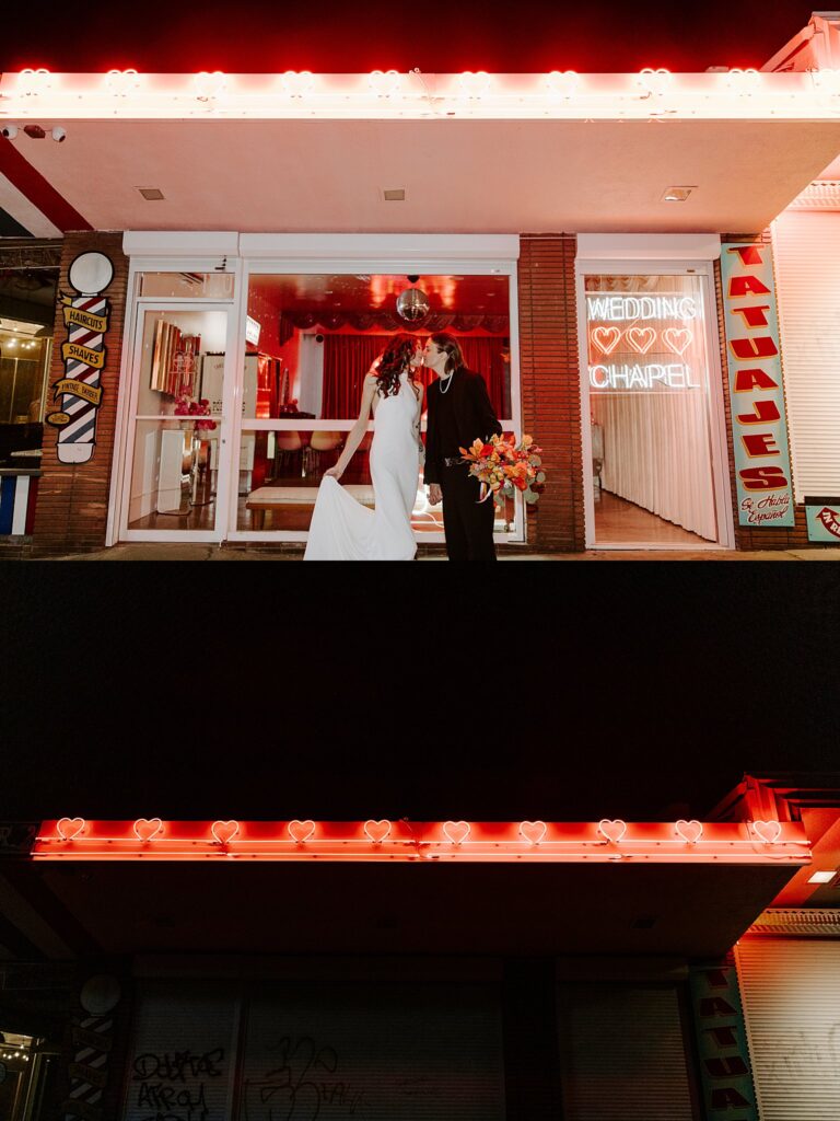 wives kiss outside chapel at night by Las Vegas wedding photographer