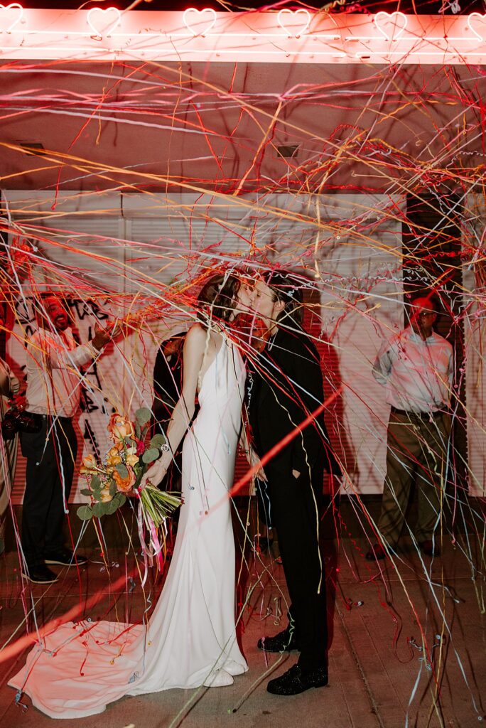 couple kisses as guests shoot streamers out at them by  Katelyn Faye Photography