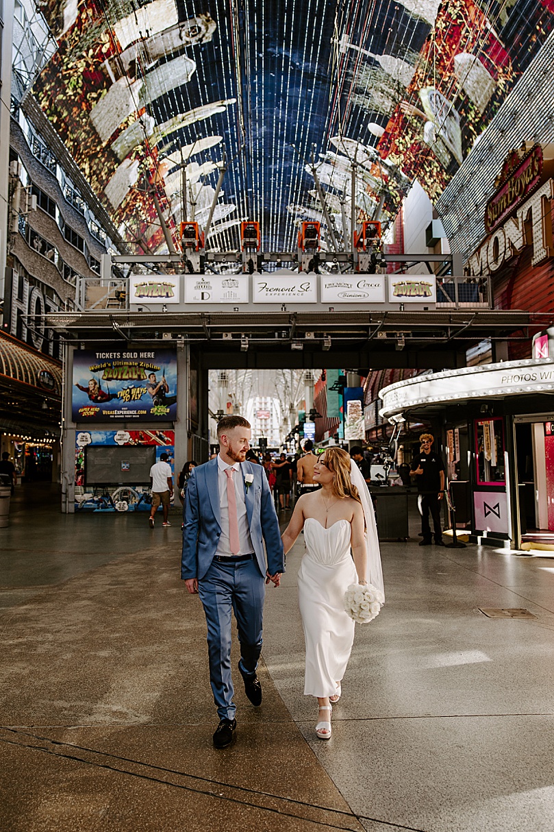 bride and groom walk down Fremont street by Las Vegas wedding photographer