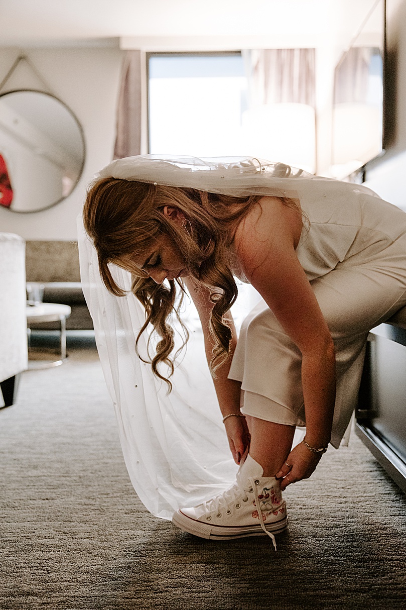 bride adjusts tennis shoe at hotel by Katelyn Faye Photo