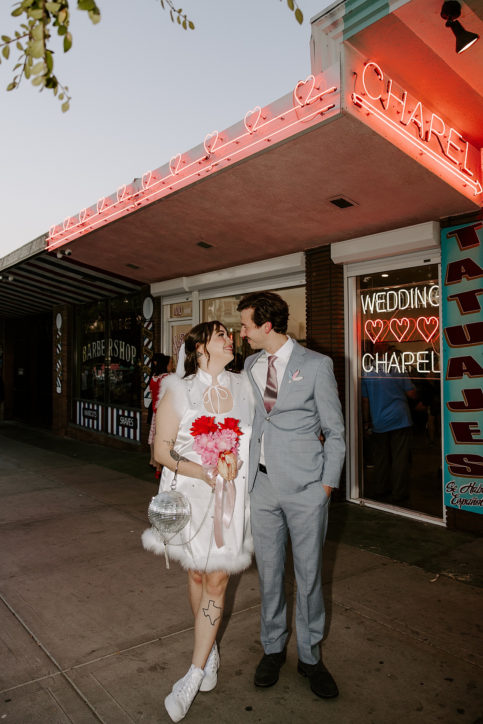 brunette in white Dress looks at groom on street by Katelyn Faye Photo