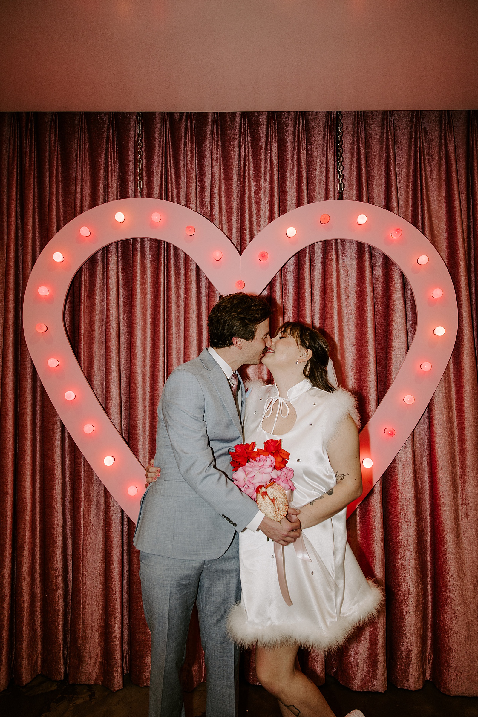 bride and groom kiss in front of neon pink heart by Las Vegas Wedding Photographer