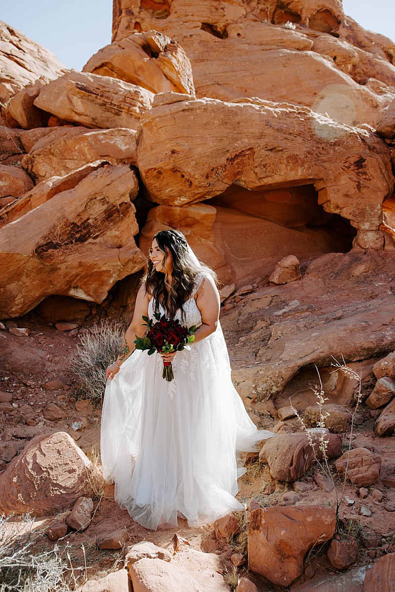 brunette bride with red flowers on red rocks by Katelyn Faye Photo