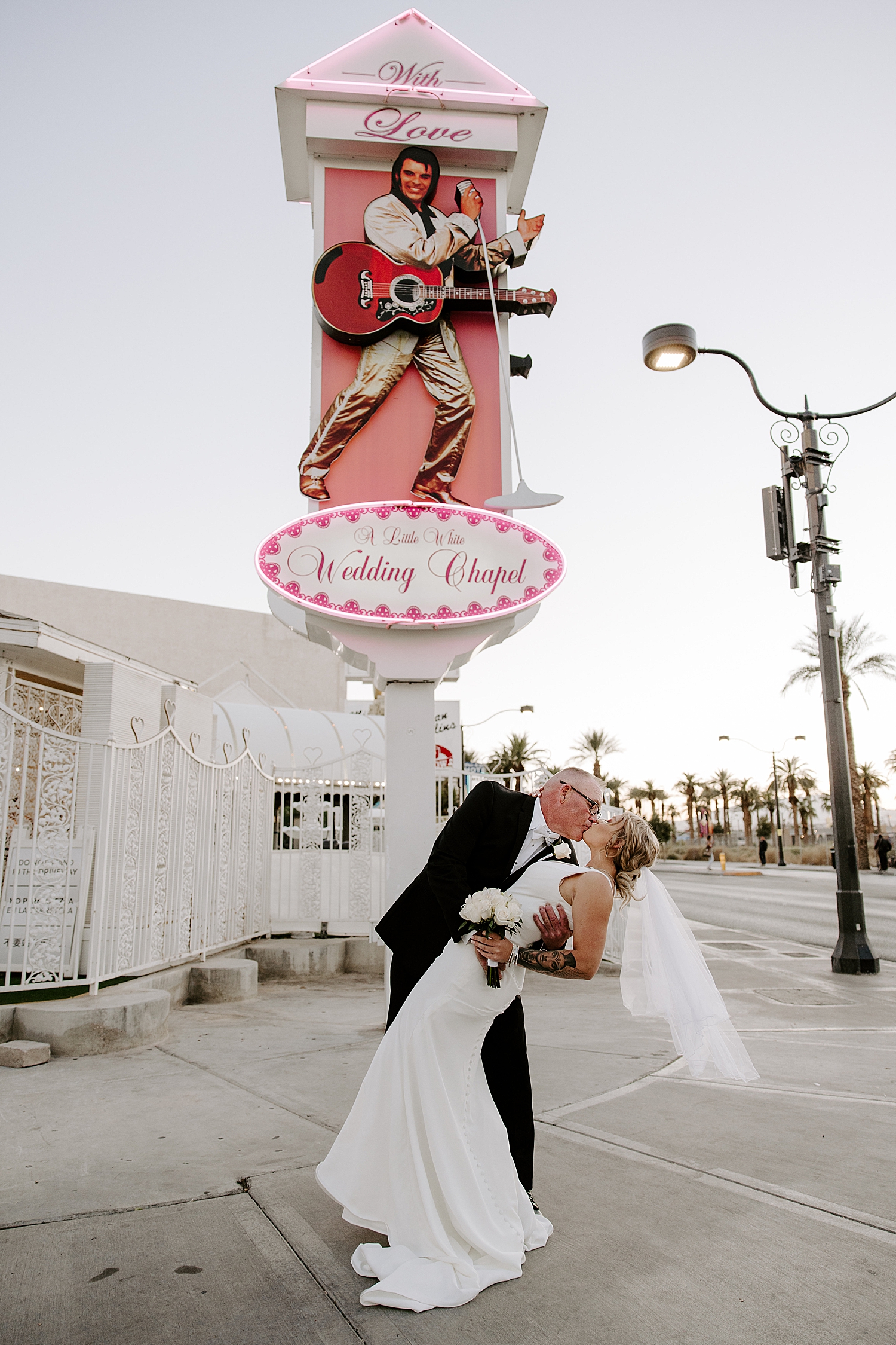 bride and groom dip for kiss under Little White Chapel sign by Las Vegas Wedding Photographer