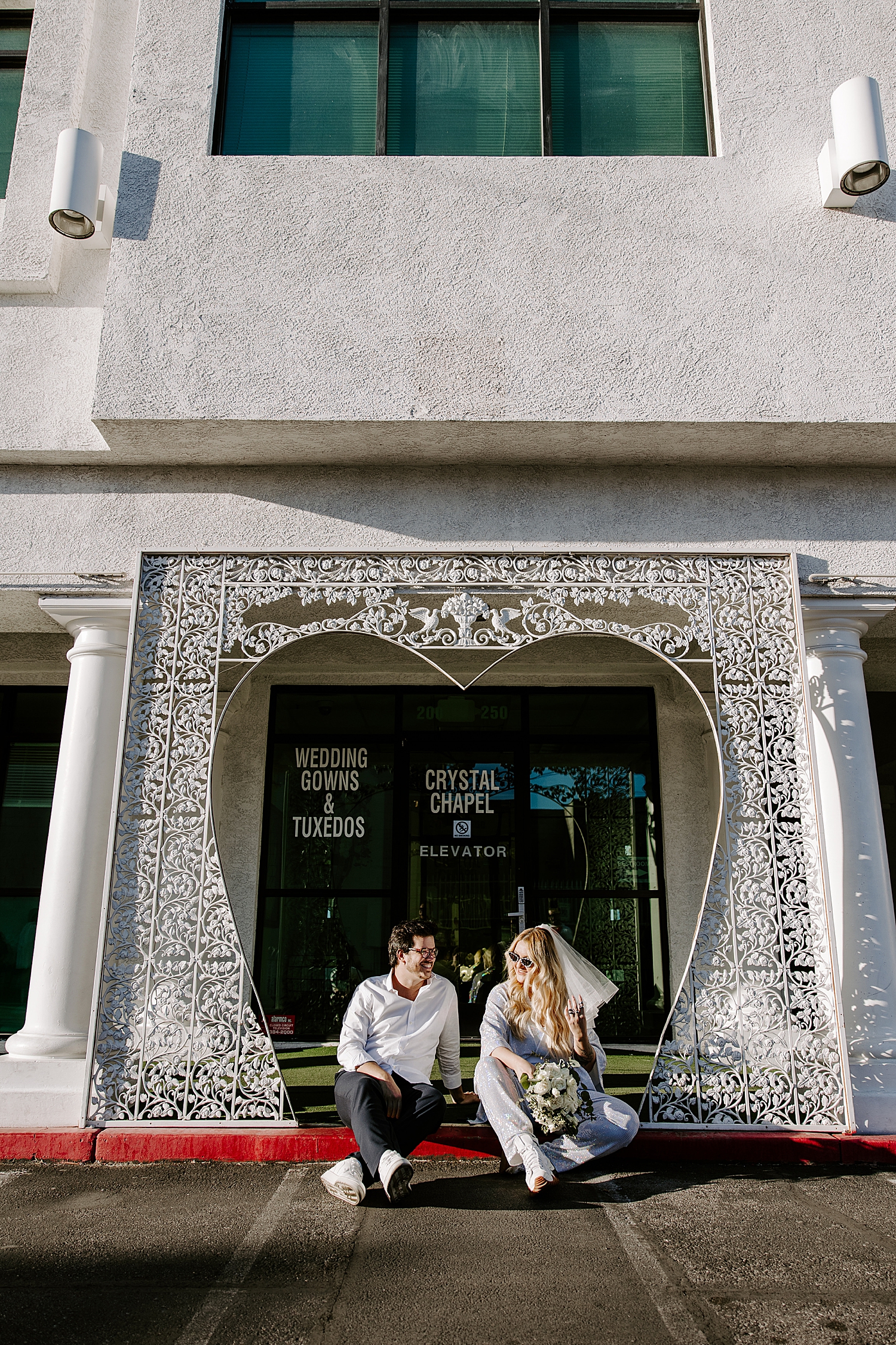 bride and groom sit on curb outside the LWC by Katelyn Faye Photo