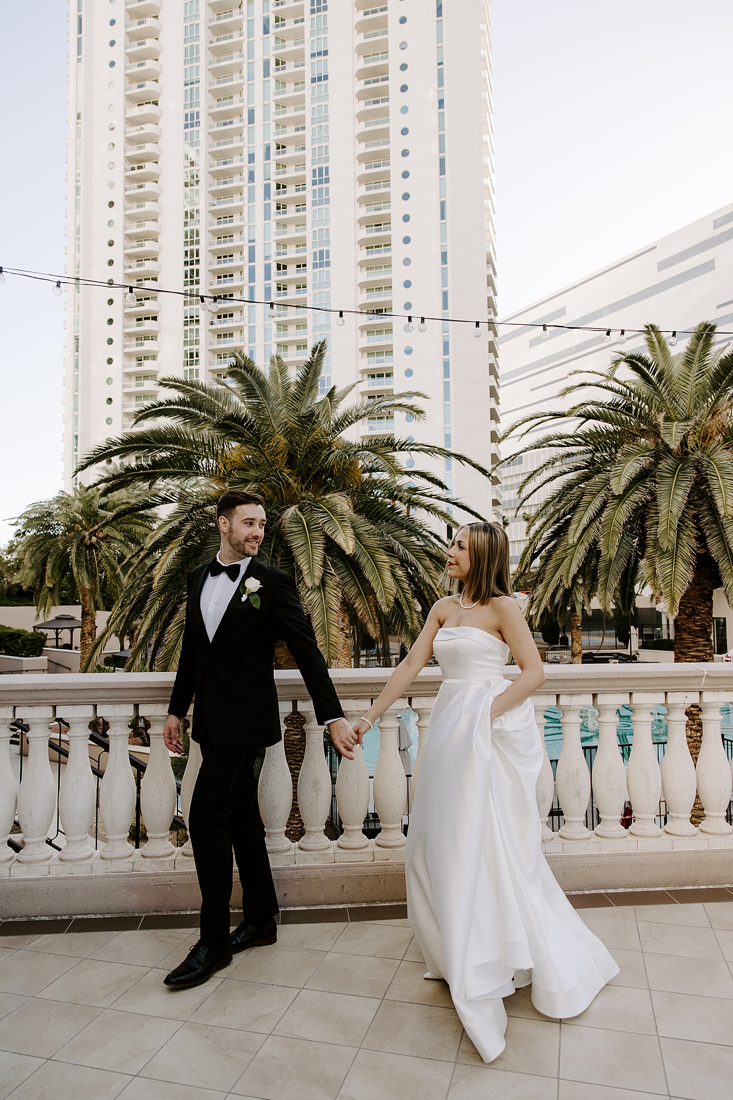 woman in white dress and man in tux walk on balcony by Katelyn Faye Photo