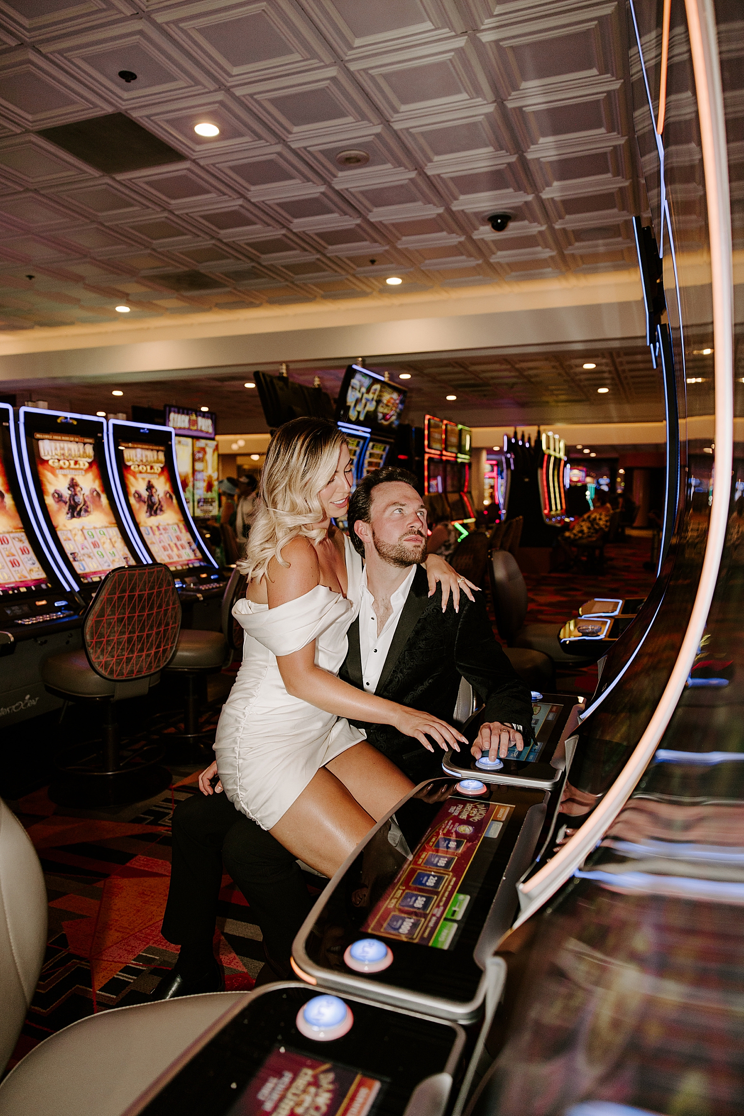woman in white dress sits on man's lap at slot machines by Las Vegas Wedding Photographer