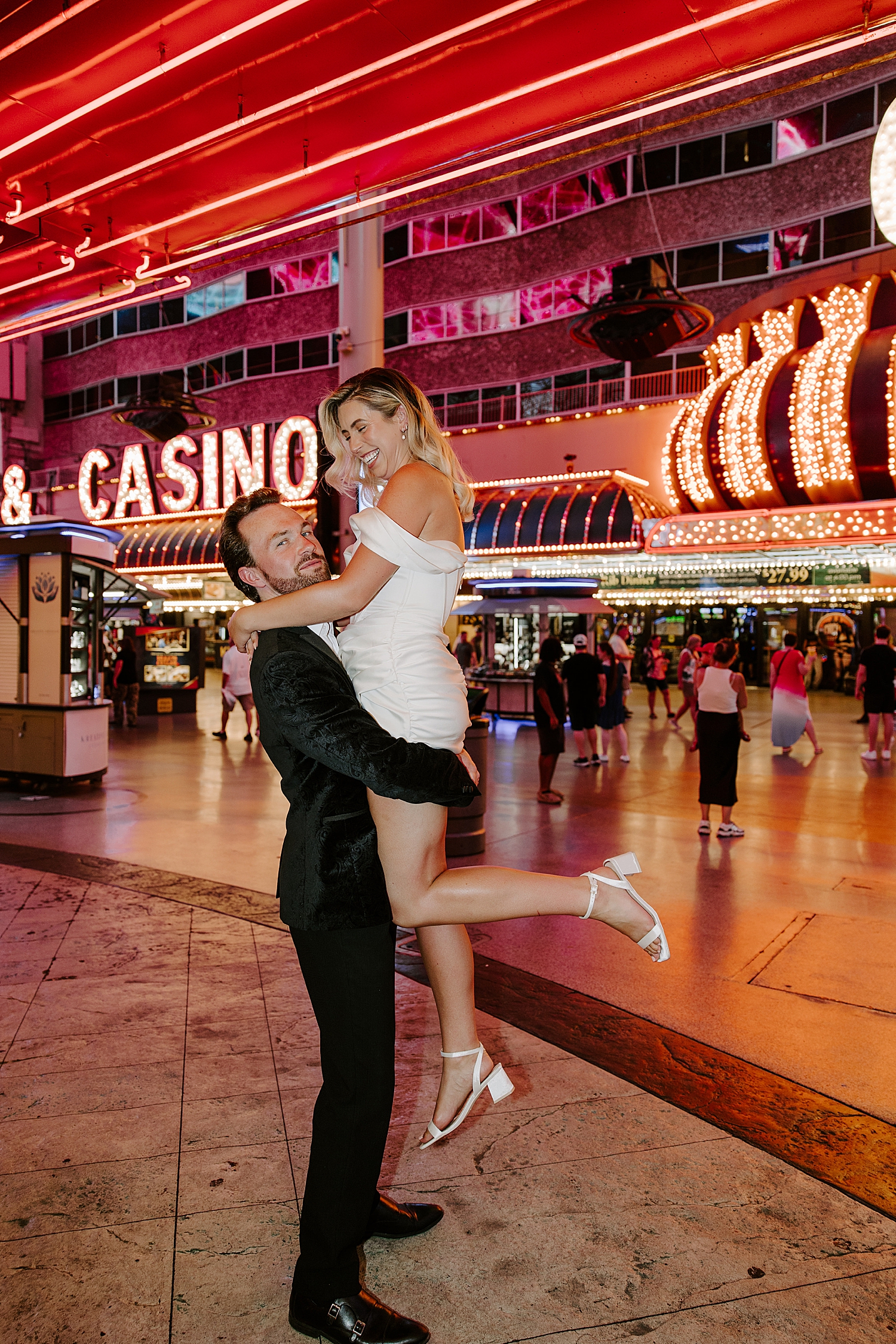 woman in white dress is lifted high by husband in front of lights for Fremont Anniversary Session