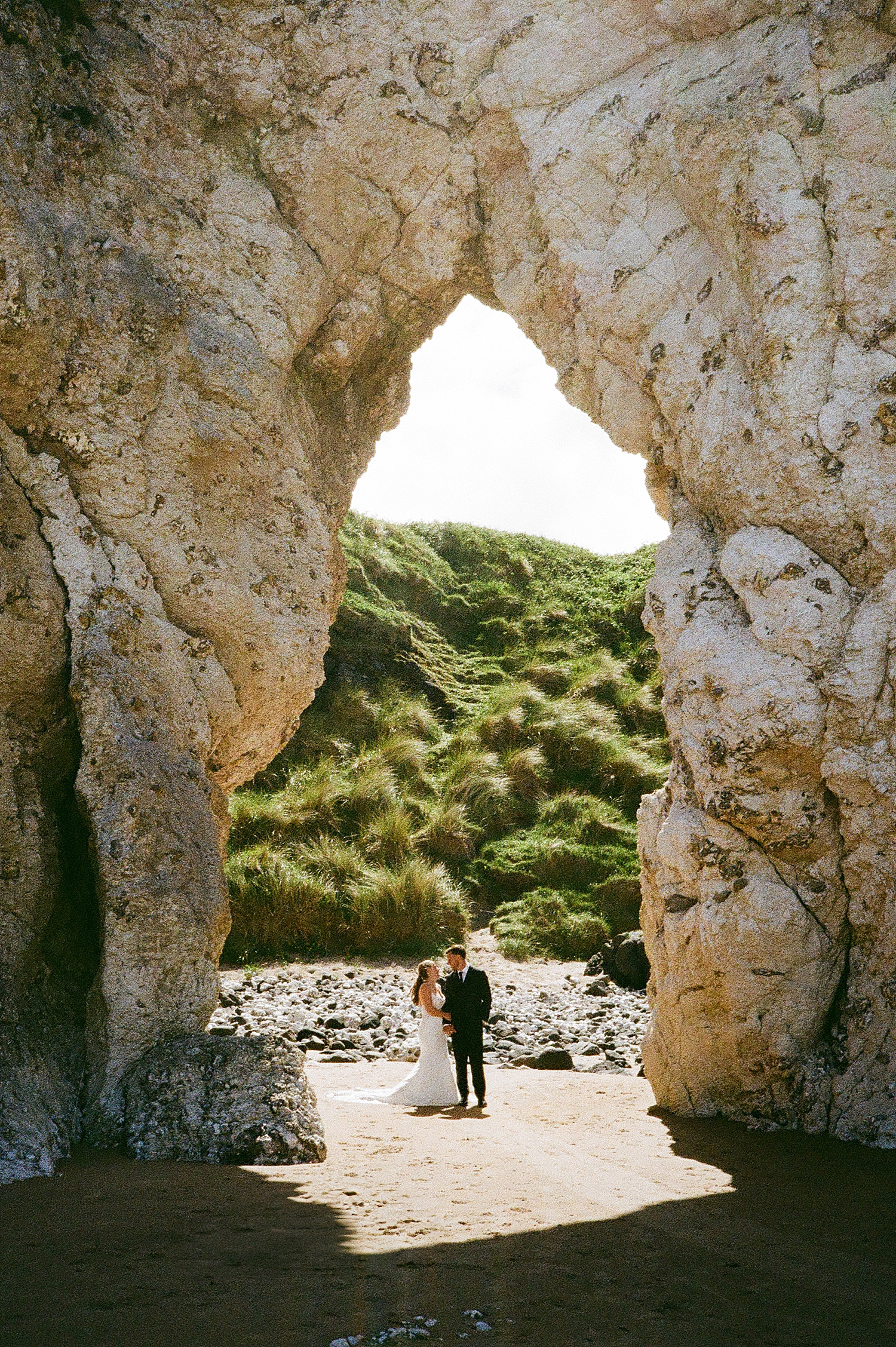 newlyweds hold hands under large rock arch by Katelyn Faye Photography