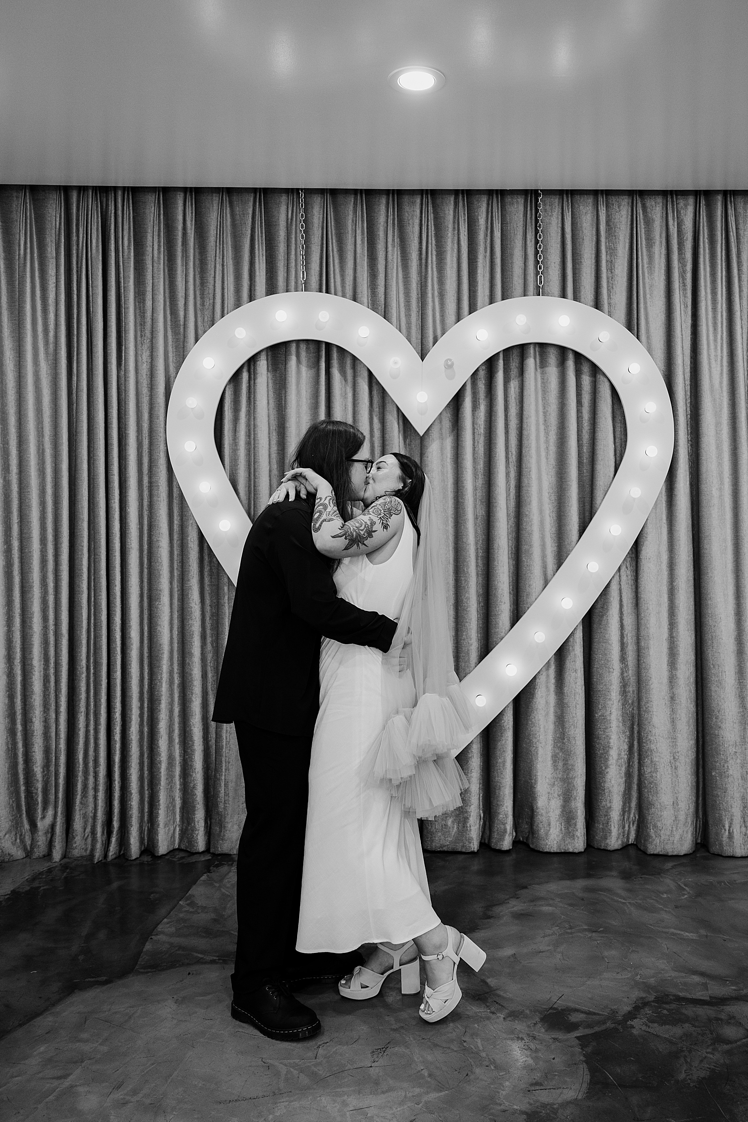 man and woman share a kiss in front of neon heart by Las Vegas wedding photographer