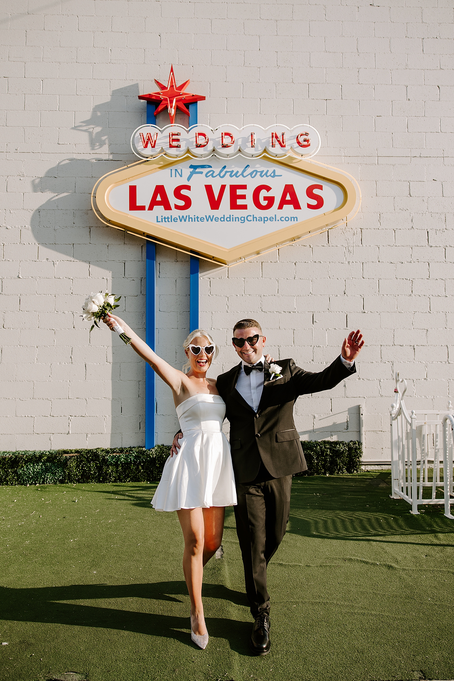 bride and groom throw hands in the air under iconic sign by Las Vegas wedding photographer