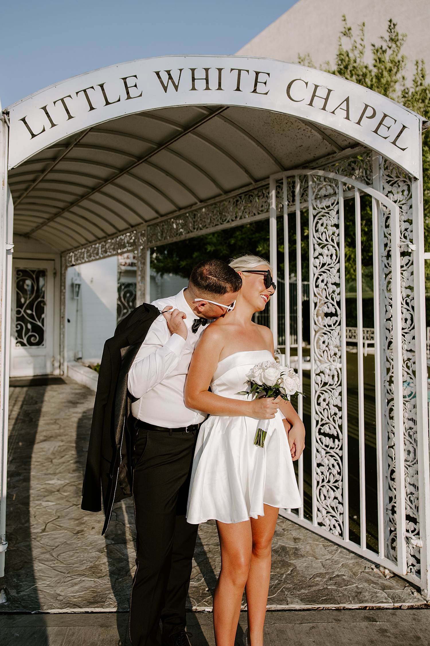 man kisses woman's neck under Little White Chapel sign by Las Vegas wedding photographer