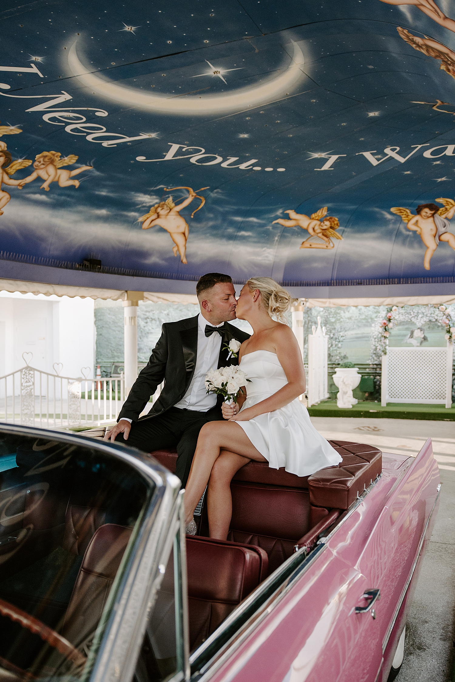 couple share a kiss sitting on the back of pink corvette in the Tunnel of Love at the LWC