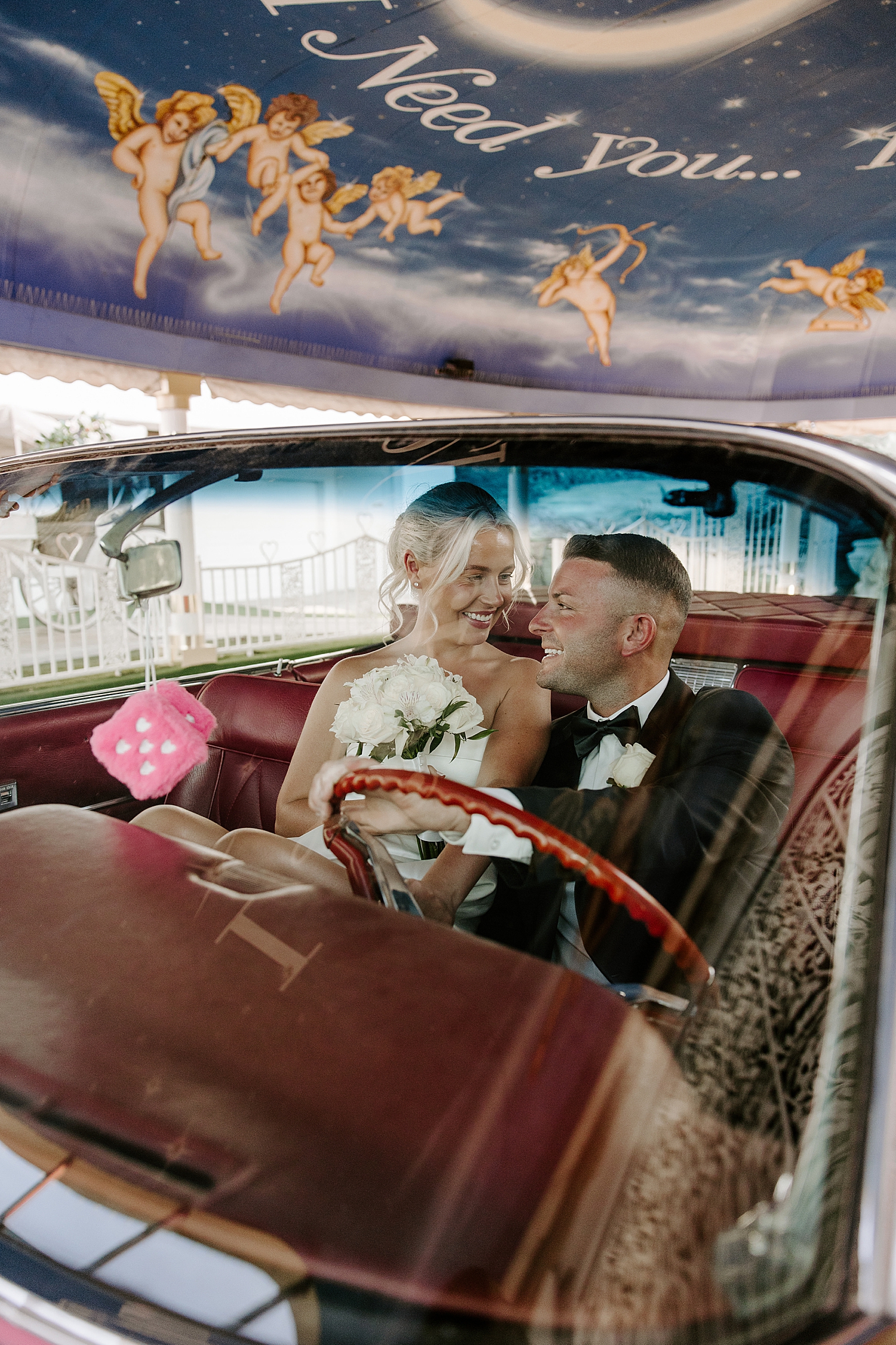 newlyweds smile at each other behind the steering wheel in Tunnel of Love