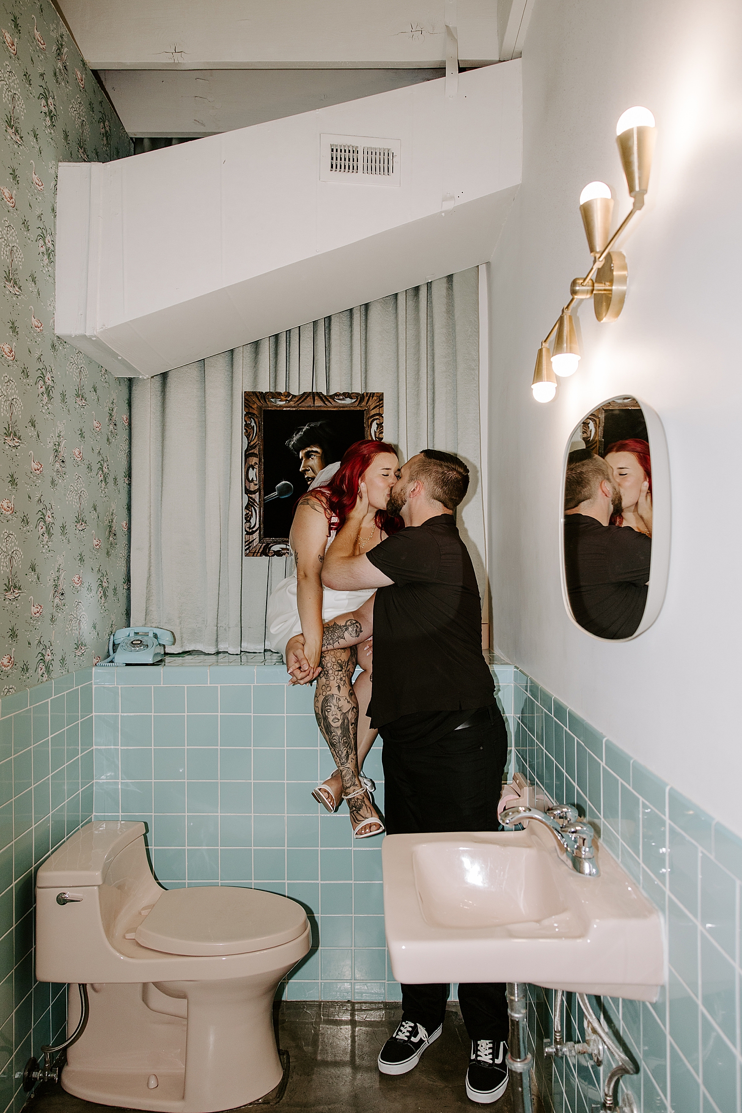 man leans in to kiss his bride sitting on blue counter by Katelyn Faye Photography