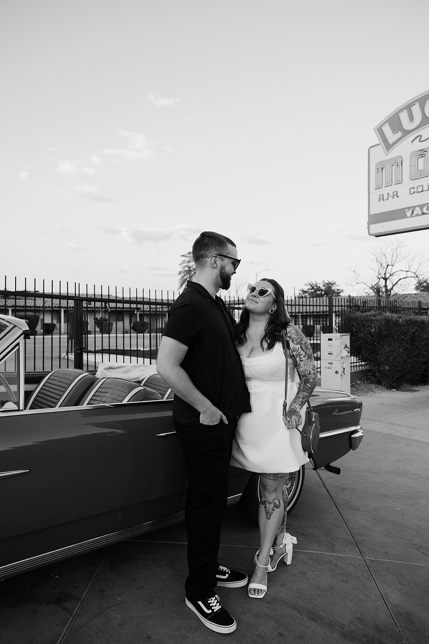husband and wife stand outside of vintage car on the street