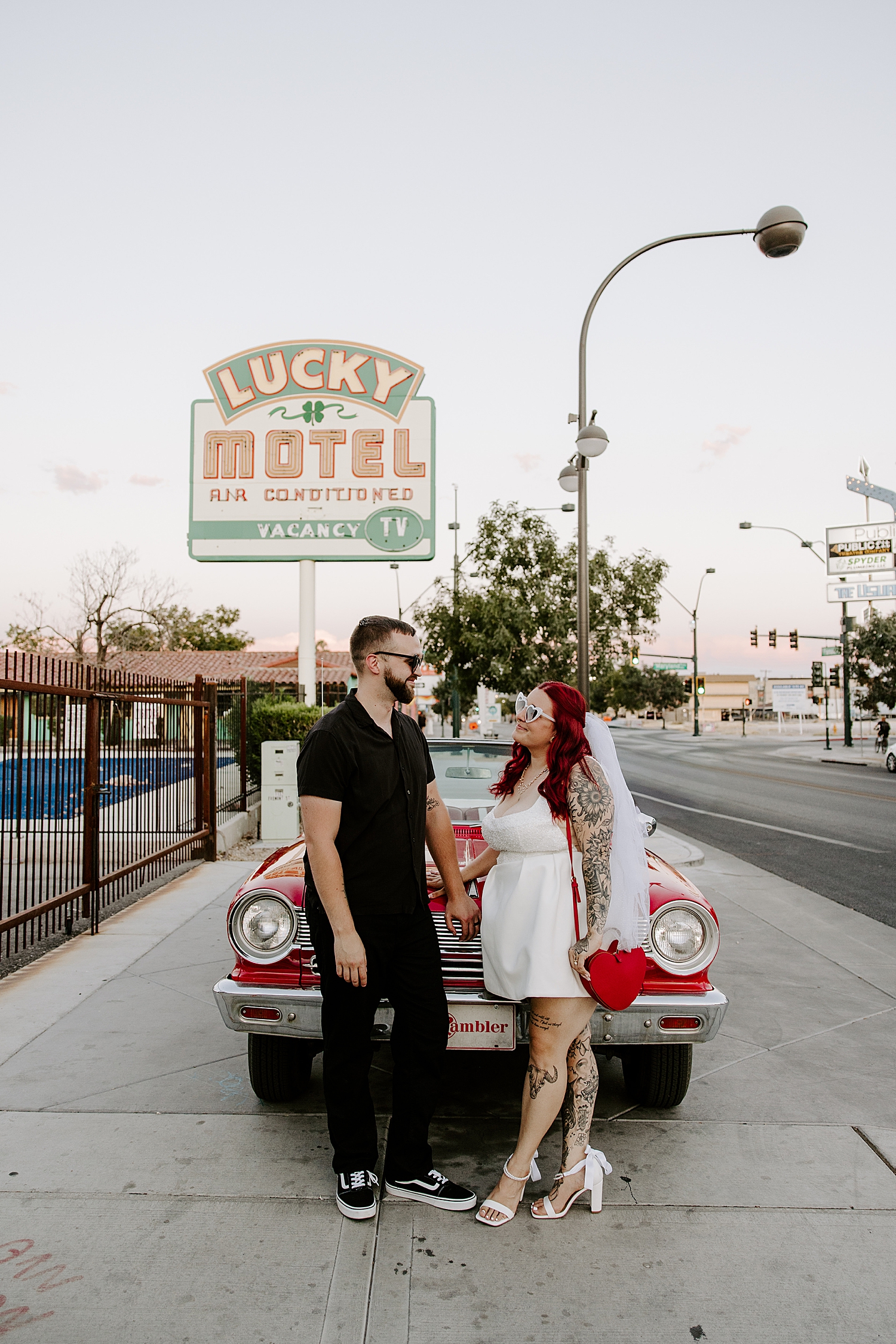 redhead with veil holds hands with her husband outside of vintage car