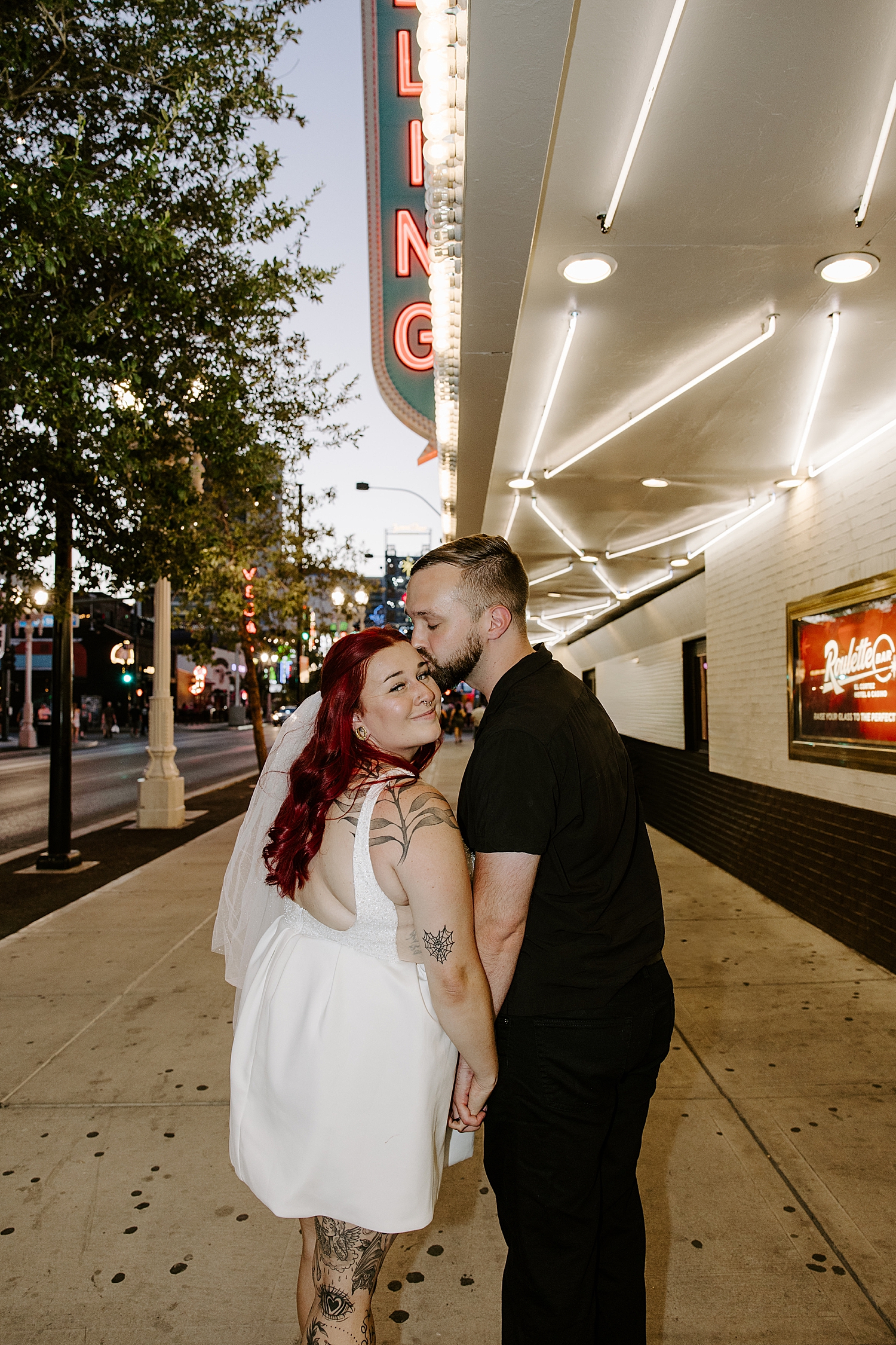 husband kisses wife's temple on busy sidewalk by Katelyn Faye Photography