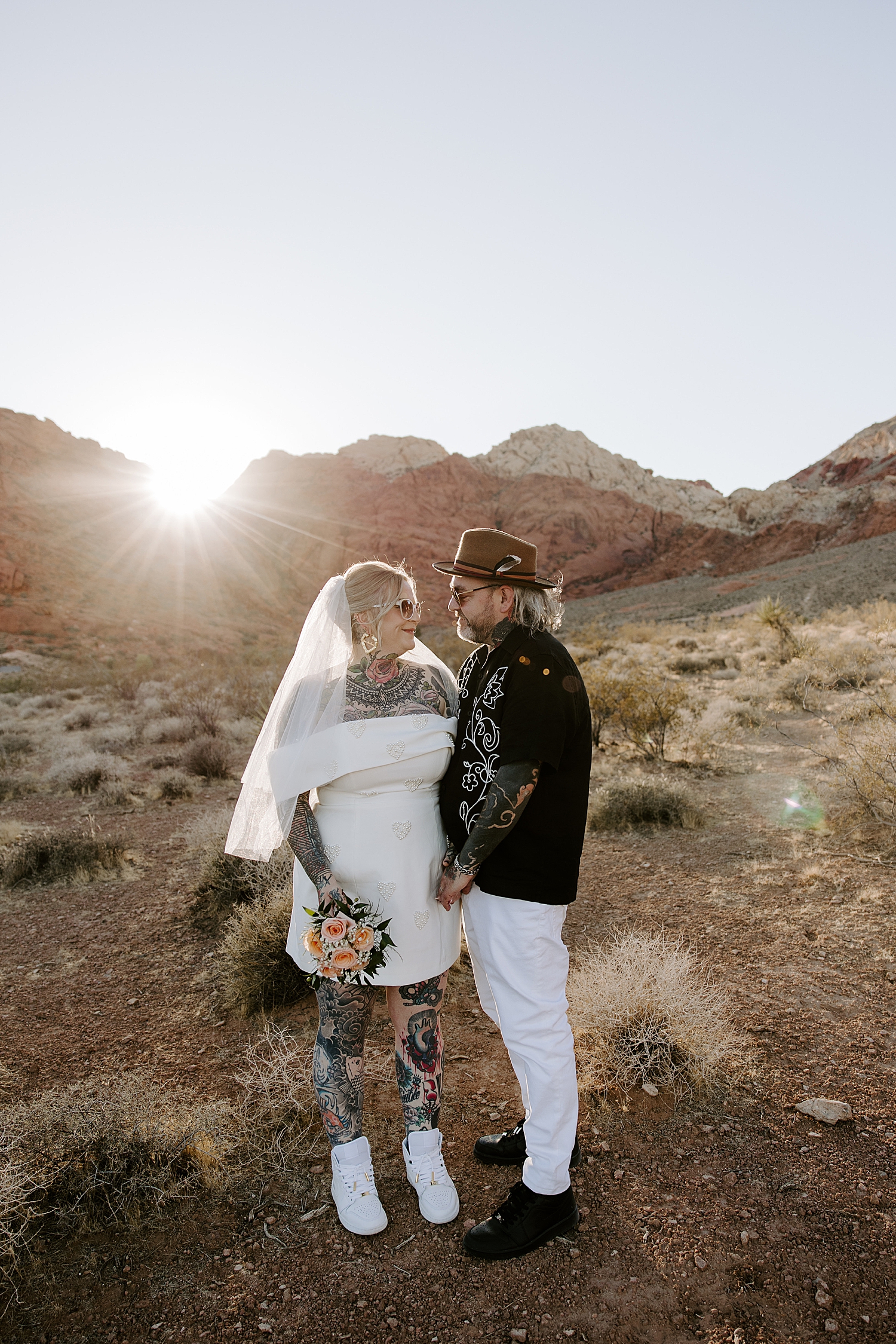 man and woman stand in front of mountains at red rocks at golden hour