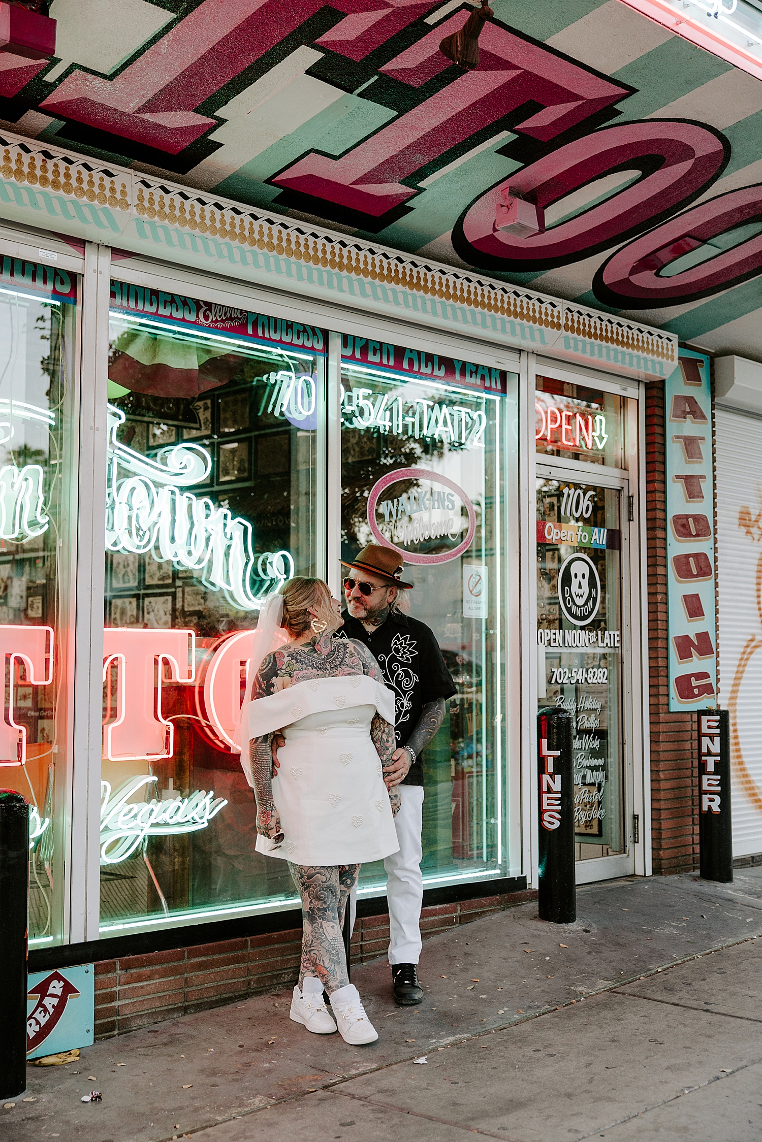 husband and wife stand on side walk in front of tattoo shop by Las Vegas Wedding Photographer
