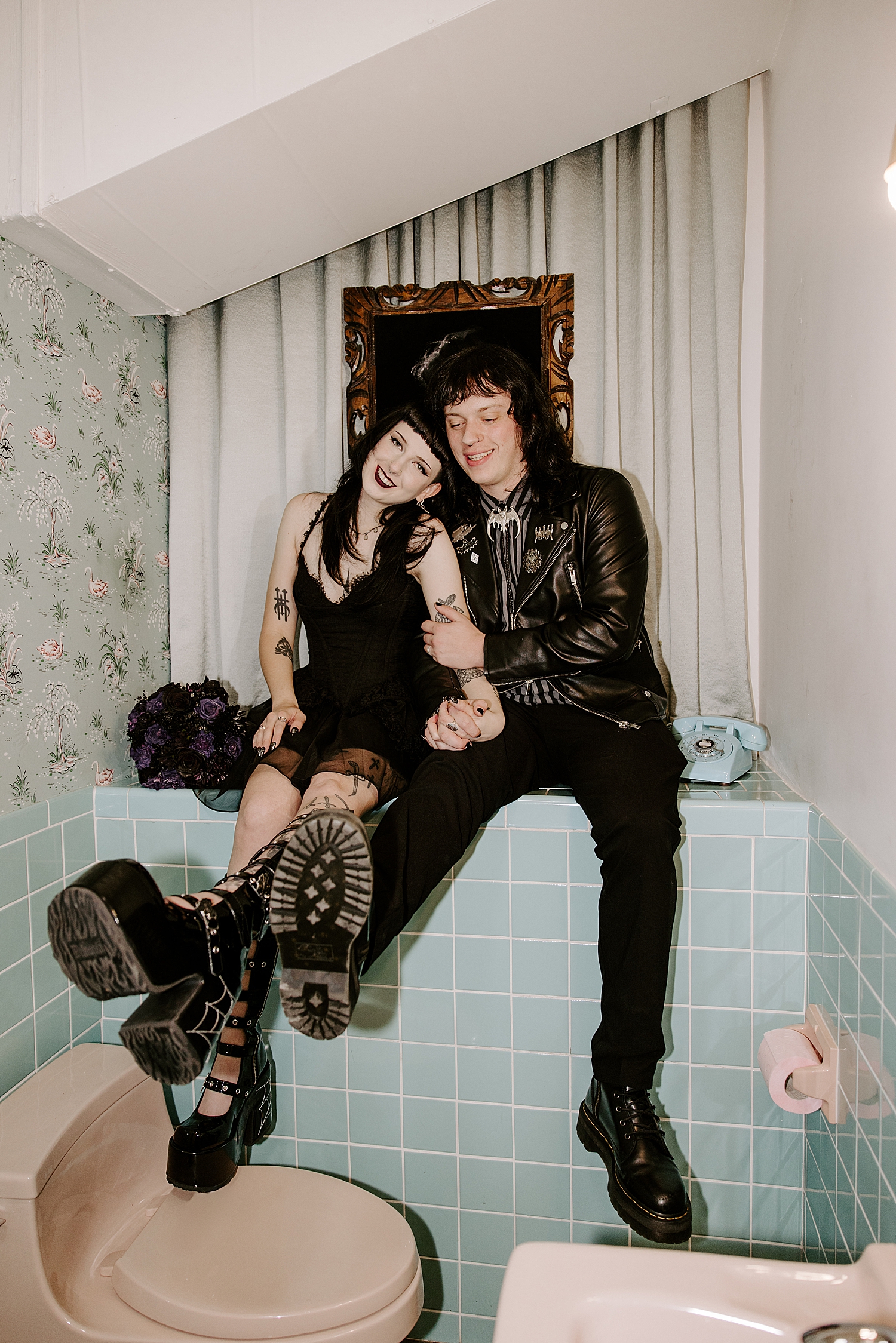 newlyweds wearing all black sit in mint color bathroom after elopement with Hellvis