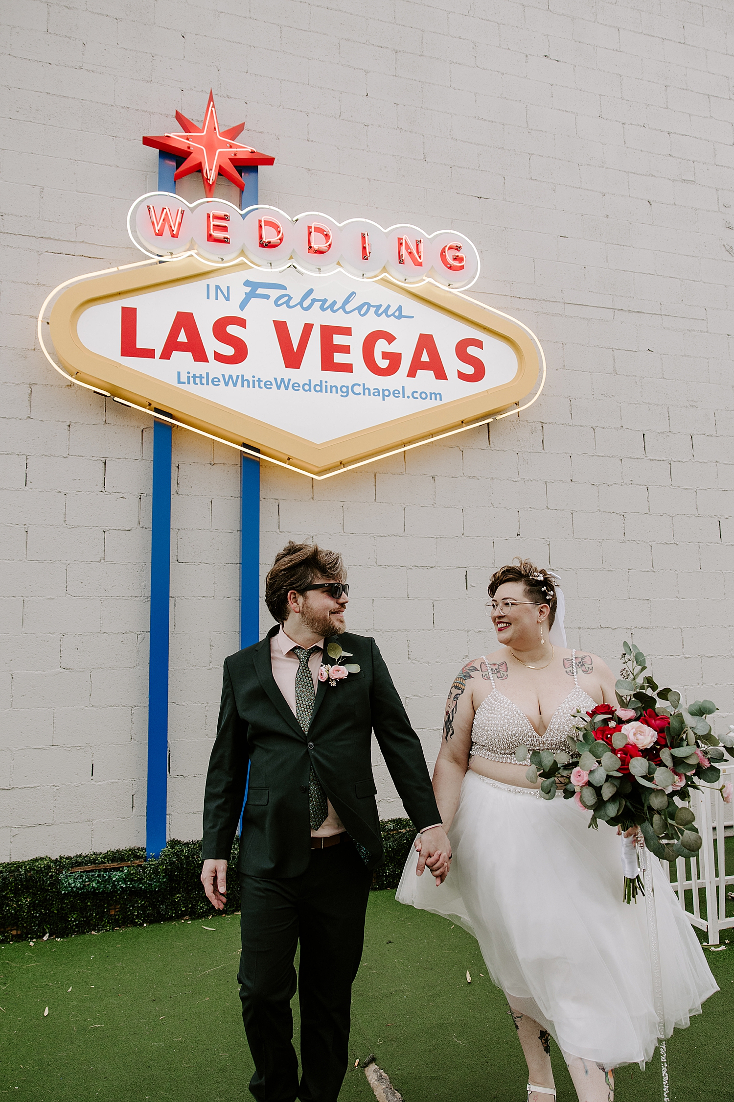 man and woman in formal attire walk in front of neon sign by Las Vegas wedding photographer