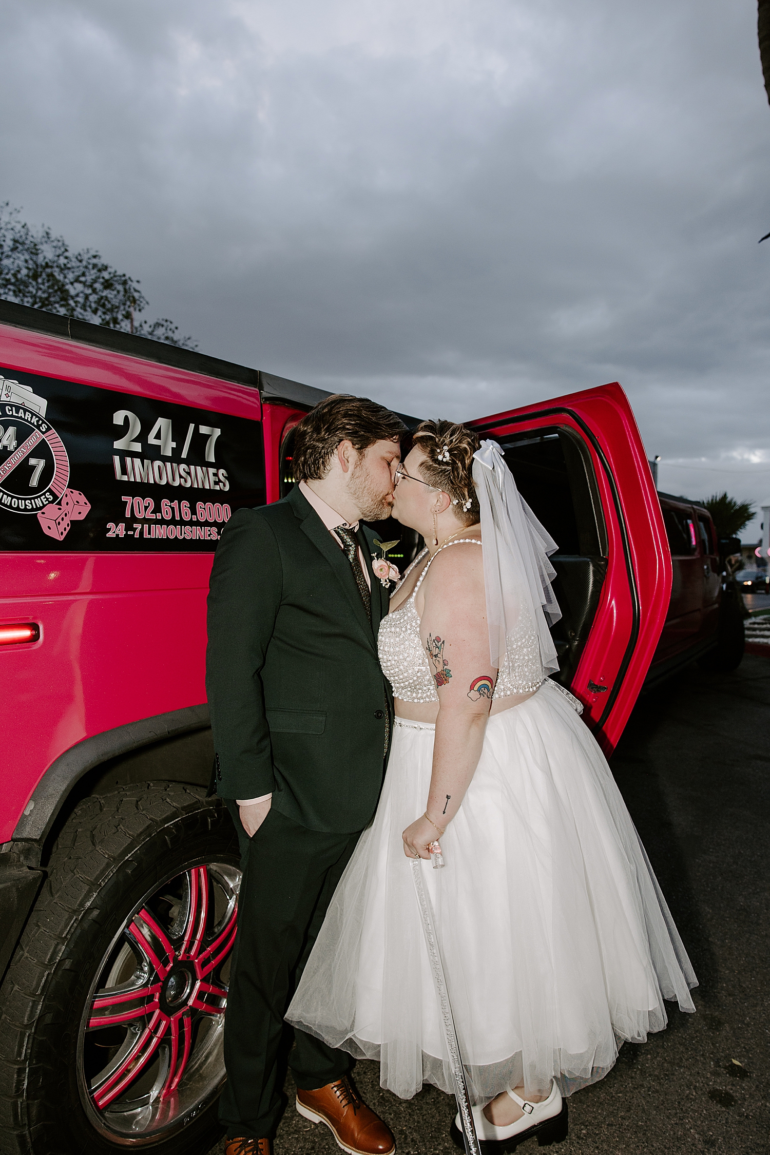 newlyweds with tattoos kiss outside of red car by Las Vegas wedding photographer