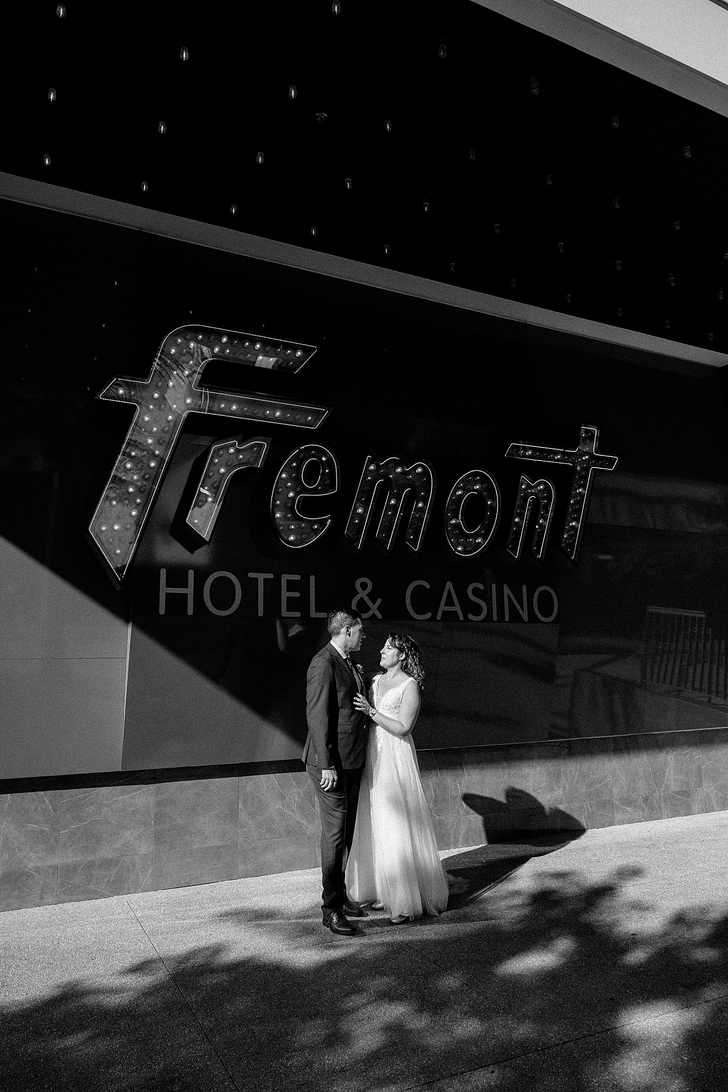 husband and wife embrace in front of light up sign by Las Vegas wedding photographer