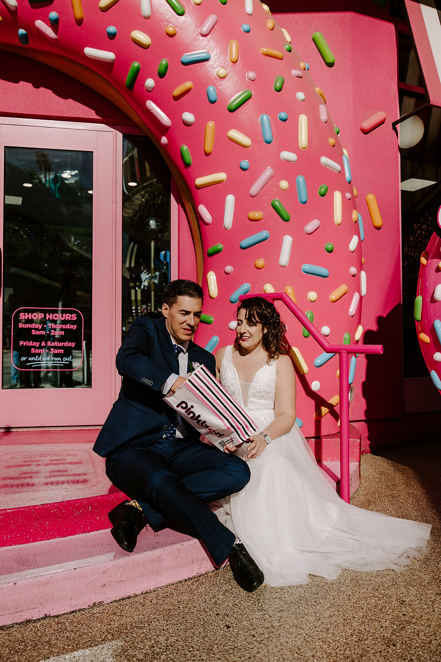newlyweds share a donut under large sprinkles arch by Las Vegas wedding photographer