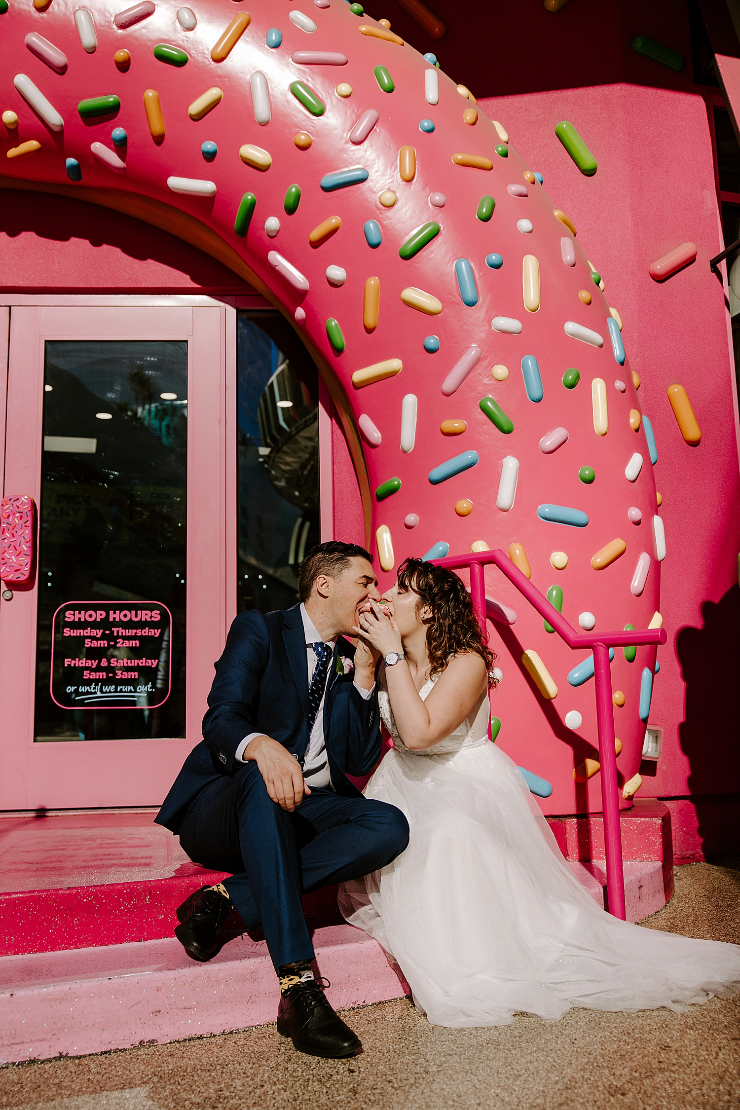 bride and groom eat a donut together under sprinkle arch by Katelyn Faye Photography